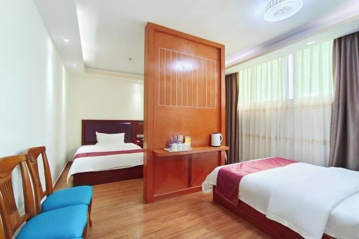 Een hotelkamer met twee bedden, een houten bureau, een stoel en een raam met gordijnen.