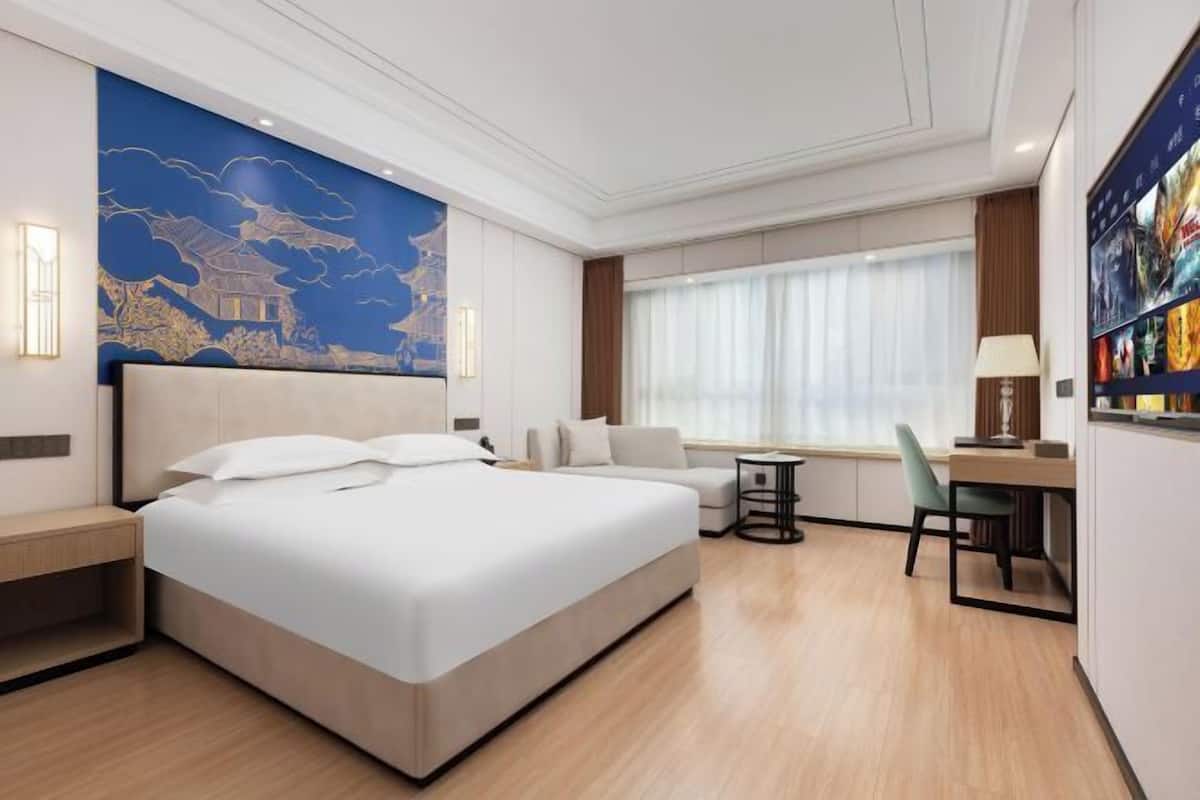 A modern hotel room with a large bed, a desk, and a seating area.