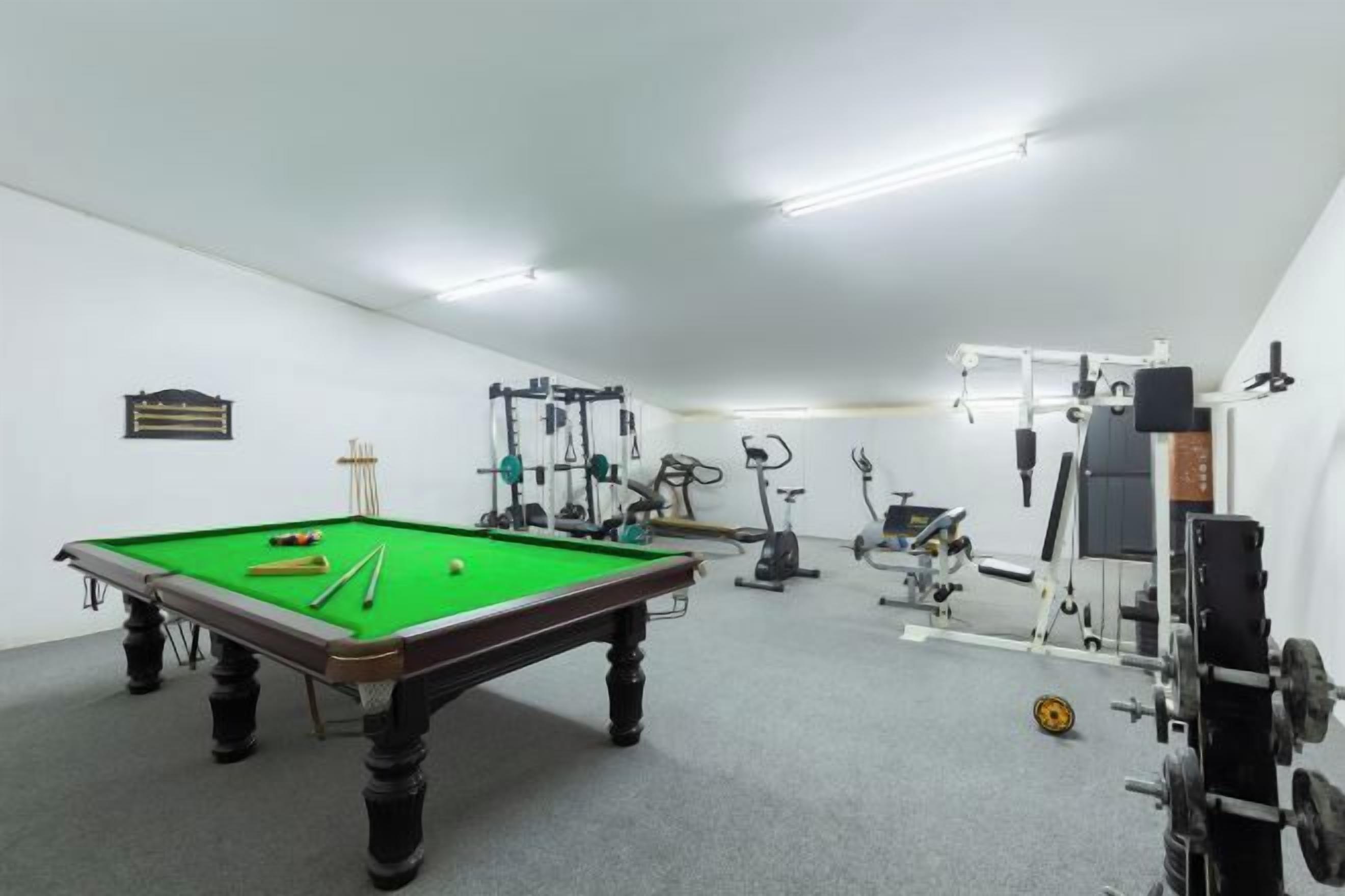 Una habitación con mesa de billar, equipo de ejercicio y una zona pequeña para jugar al billar.