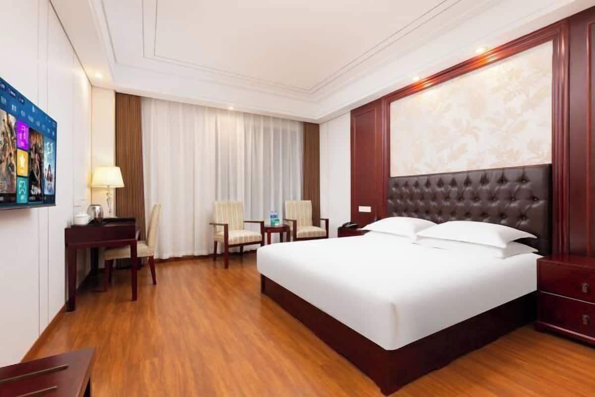A hotel room with a large bed, a desk with a chair, a small table, and a television.