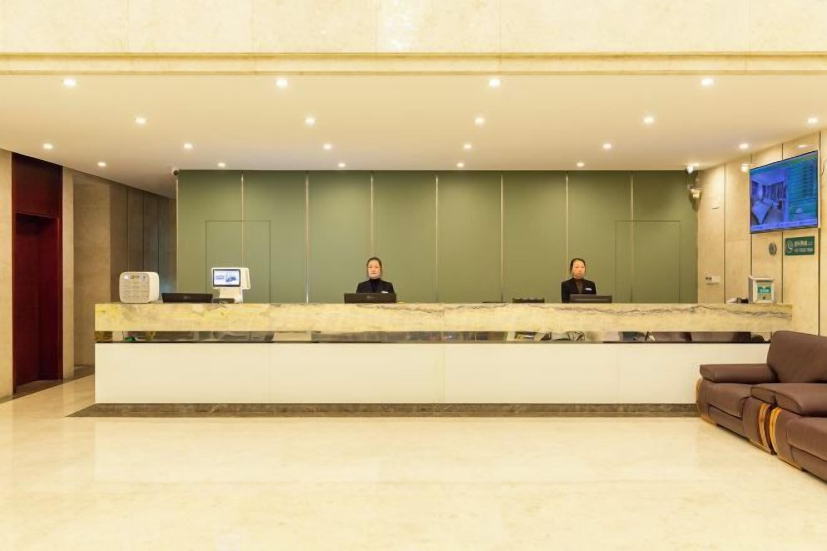 Zona de recepción de un hotel con dos recepcionistas, una barra de mármol y una pantalla de televisión.