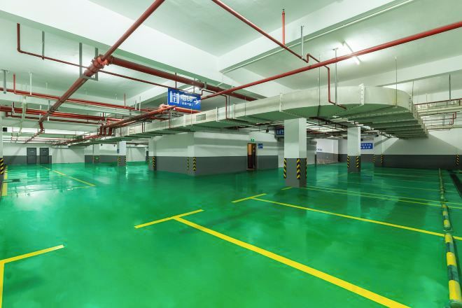 A spacious indoor parking area with clear yellow lines marking parking spaces, red pipes on the ceiling, and a blue sign indicating the exit.