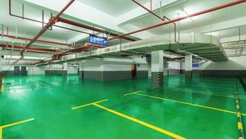 A spacious indoor parking area with clear yellow lines marking parking spaces, red pipes on the ceiling, and a blue sign indicating the exit.
