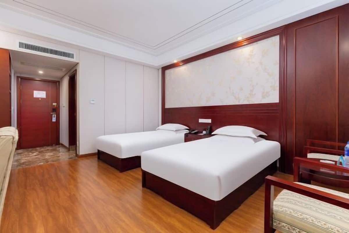 A hotel room with two single beds, wooden flooring, a wooden headboard, and a small table with a chair.