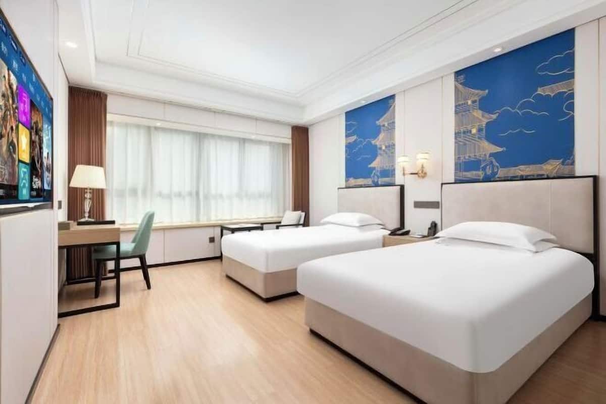 A hotel room with two beds, a desk, a chair, and a large window with curtains.