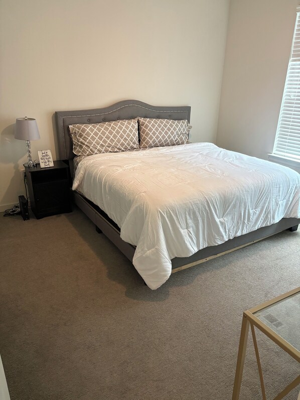 A bedroom with a bed, a nightstand, a lamp, and a window with blinds.