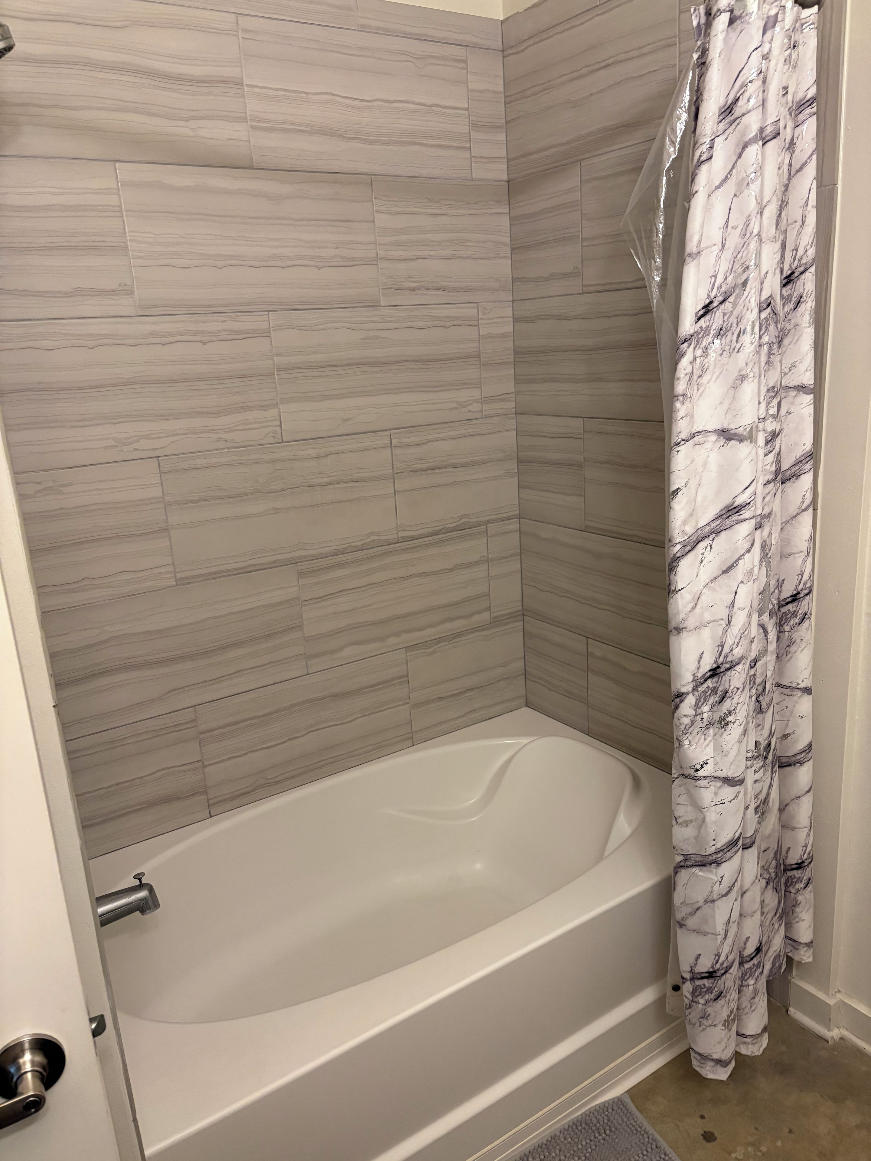 A bathroom with a bathtub, shower curtain, and tiled walls.