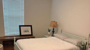 A bedroom with a large bed, bedside tables, a lamp, a framed picture, and a window with blinds.