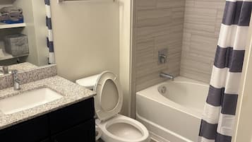 A bathroom with a toilet, sink, bathtub, shower, and a striped shower curtain.