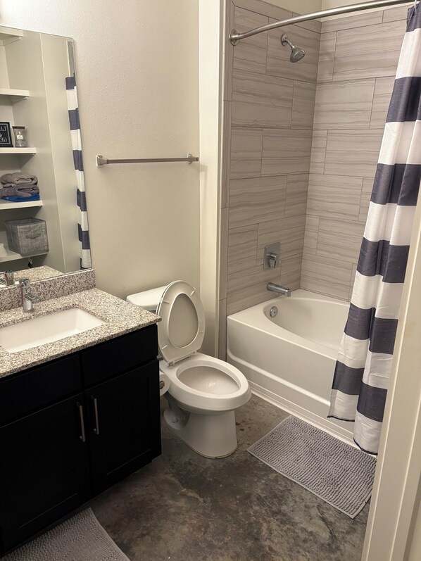A bathroom with a toilet, sink, bathtub, shower, and a striped shower curtain.