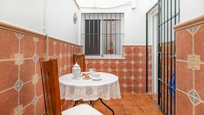 A small patio with a round table, chairs, and a white tablecloth. There is a window with metal bars and a door with a metal gate. - 2 bedroom nice apartment in Chipiona (Chipiona)