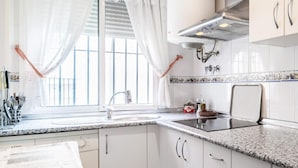 A modern kitchen with white cabinetry, a granite countertop, a window with white curtains, and a stainless steel range hood. - 2 bedroom nice apartment in Chipiona (Chipiona)