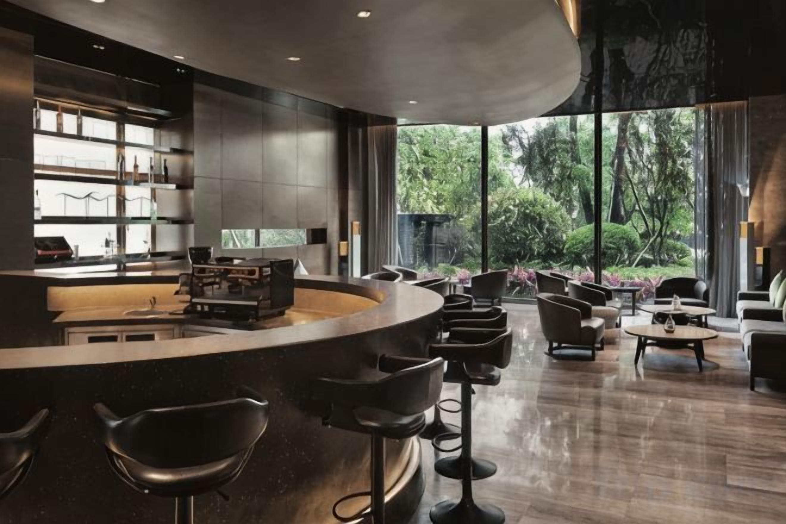 A modern bar area with a curved counter, bar stools, and a view of the outdoors through large windows.