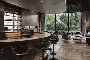 A modern bar area with a curved counter, bar stools, and a view of the outdoors through large windows.