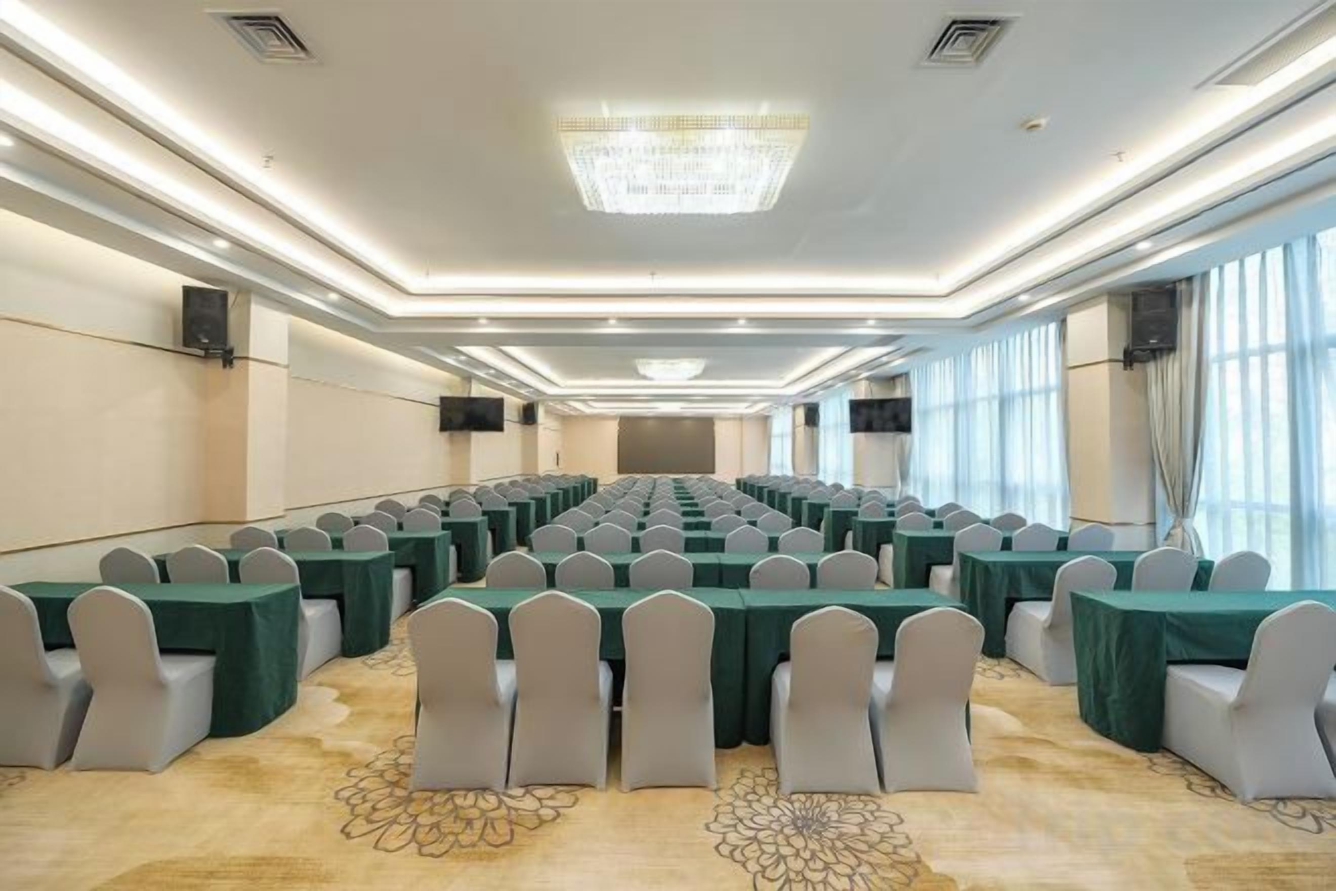 A conference room with rows of tables and chairs, large windows, and a chandelier.