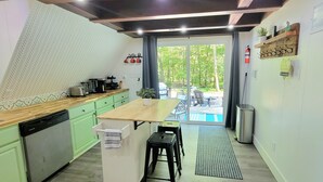 Eine Küche mit Holzarbeitsplatte, grünen Schränken und Blick auf einen Garten mit Pool.