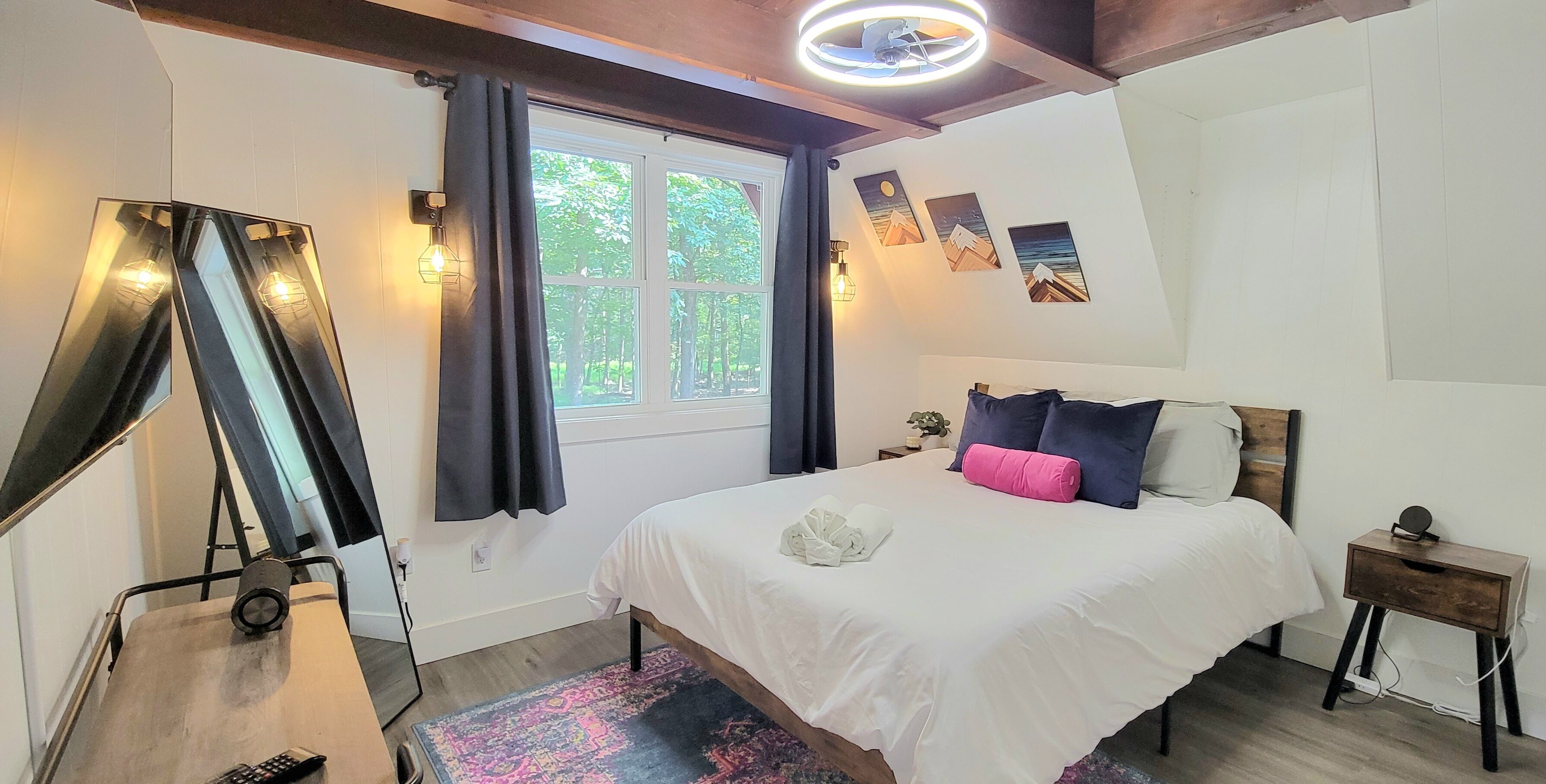 Een slaapkamer met een bed, een spiegel, een raam met gordijnen, wandlampen en kunstwerken.