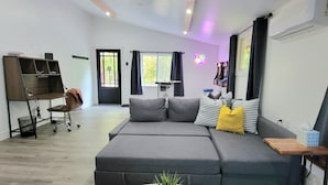 Ein modernes Wohnzimmer mit einem grauen Sofa, einem kleinen Holztisch, einem schwarzen Bürostuhl und einem schwarzen Metallregal.