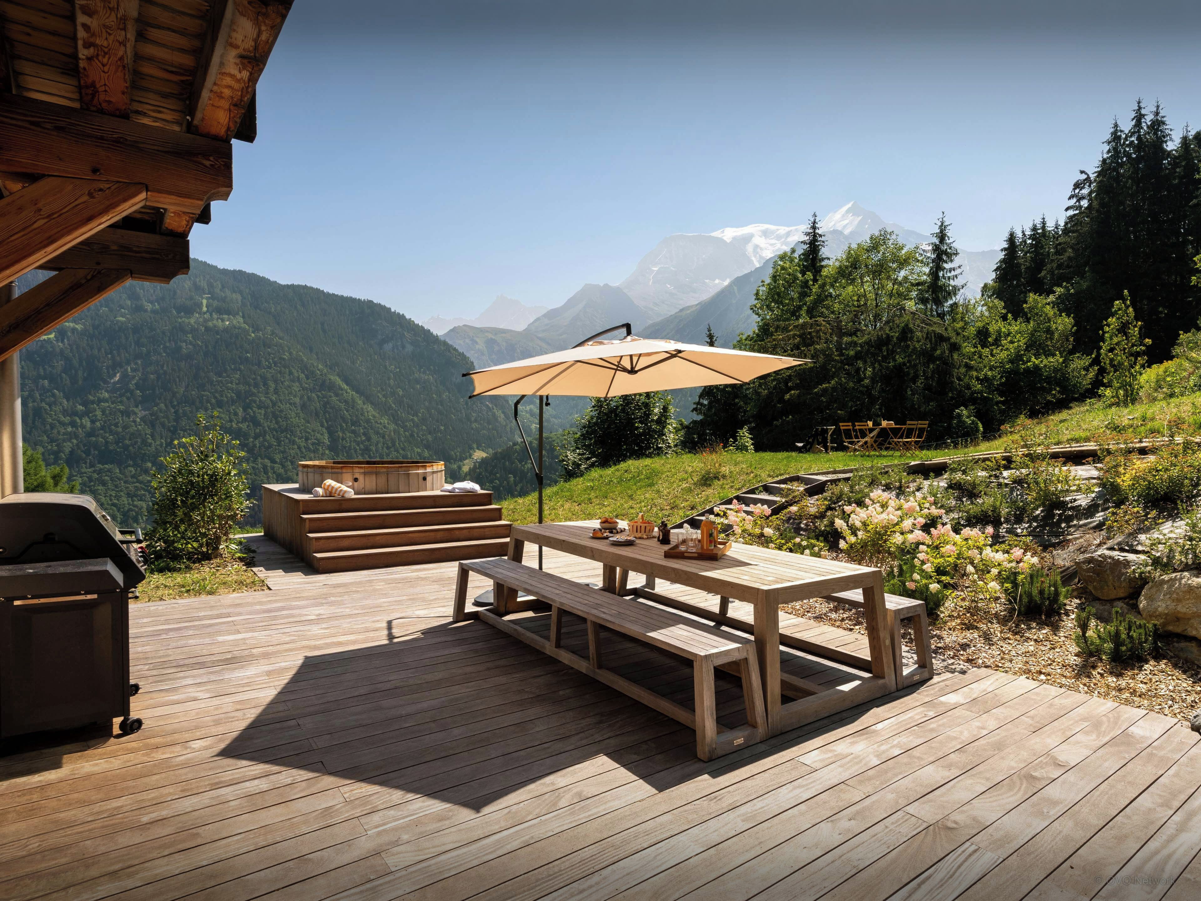A wooden deck with a table and benches, overlooking a mountainous landscape.