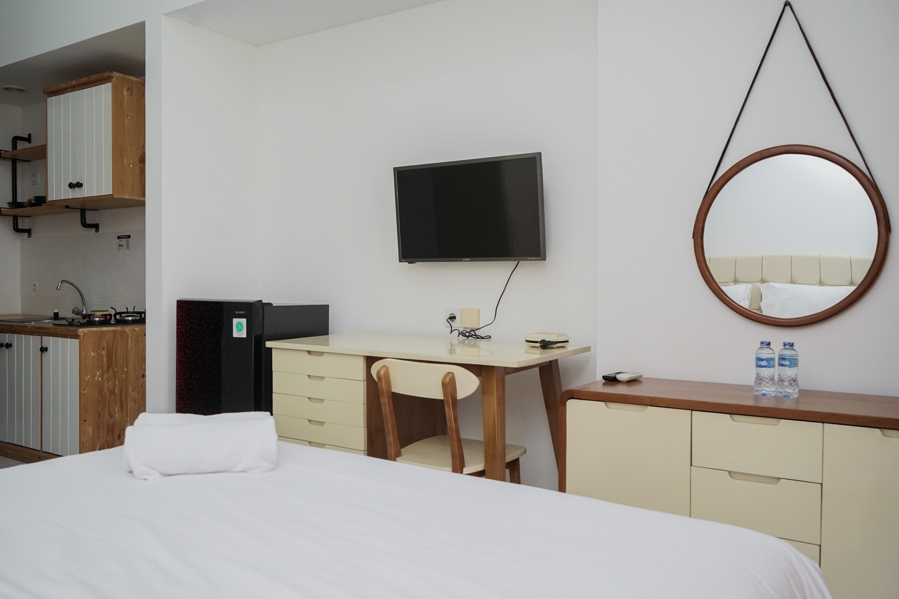 Ein Hotelzimmer mit Bett, Schreibtisch, Stuhl, Fernseher, Spiegel, Kleiderschrank und einer Küchenzeile.