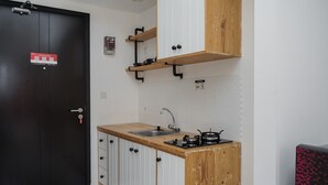 A compact kitchen with a wooden countertop, a sink, and a stove. There is a black door with a red sign, and a white textured wall. - Simple And Warm Studio At Casa De Parco Apartment (Pagedangan)