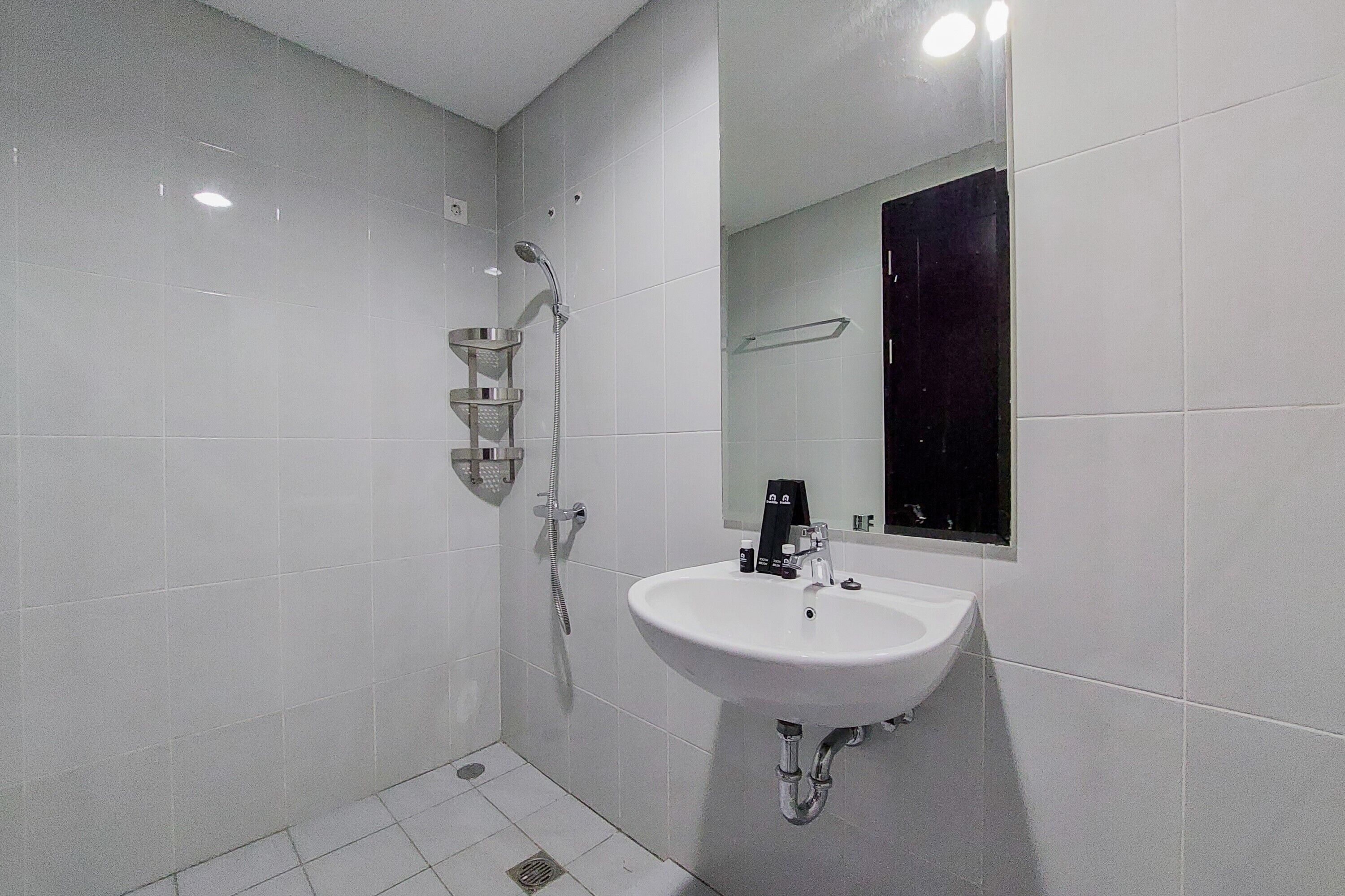 A modern bathroom with white tiles, a white sink, a mirror, and a shower with a handheld showerhead.