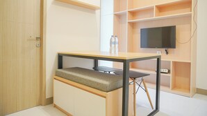 A compact room with a foldable desk, a bench, a television on a shelf, and a water bottle on the desk. - Comfort Designed 2Br At Tokyo Riverside Pik 2 Apartment (Teluknaga)