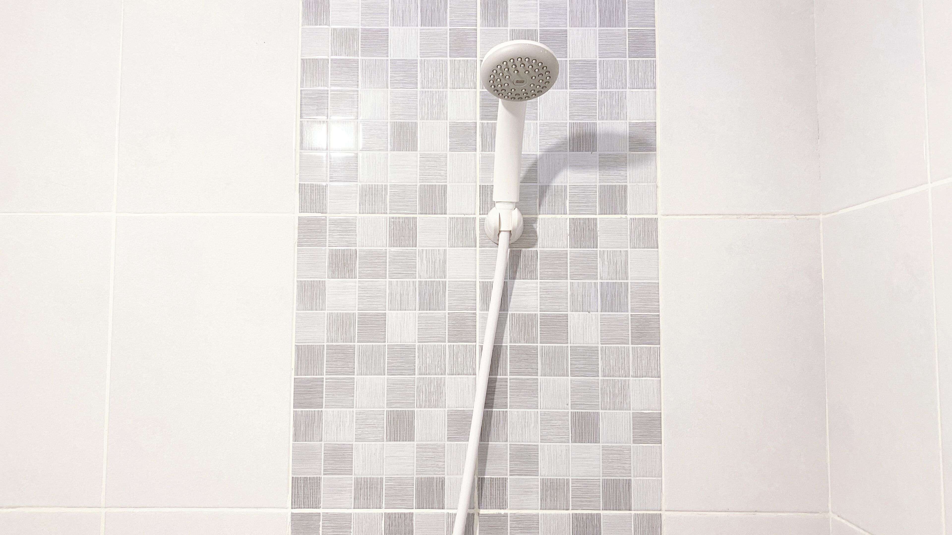 Ducha con cabezal de ducha de mano frente a una pared de azulejos.