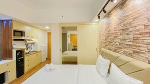 A hotel room with a bed, a kitchenette, a bathroom, and a stone wall. - Minimalist and Cozy Studio LRT City Jatibening Apartment (Bekasi)