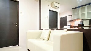 Un salon moderne avec un canapé blanc, une porte fermée et un coin cuisine à l’arrière-plan.