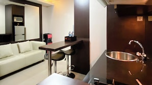 Une chambre d’hôtel compacte comprenant un coin cuisine, un canapé blanc, une petite table avec des chaises et un miroir.
