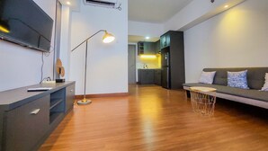 A modern living room with a flat-screen TV, a standing lamp, a sofa, and a round coffee table. - Comfy And Minimalist 1Br At Tamansari Bintaro Mansion Apartment (South Tangerang)