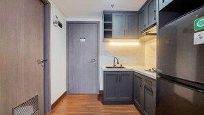 A narrow kitchen with dark cabinets, a stainless steel refrigerator, and a marble countertop. - Comfy And Minimalist 1Br At Tamansari Bintaro Mansion Apartment (South Tangerang)