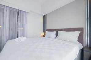 A neatly made bed with white linens, a headboard, and a bedside lamp. - Comfy And Minimalist 1Br At Tamansari Bintaro Mansion Apartment (South Tangerang)
