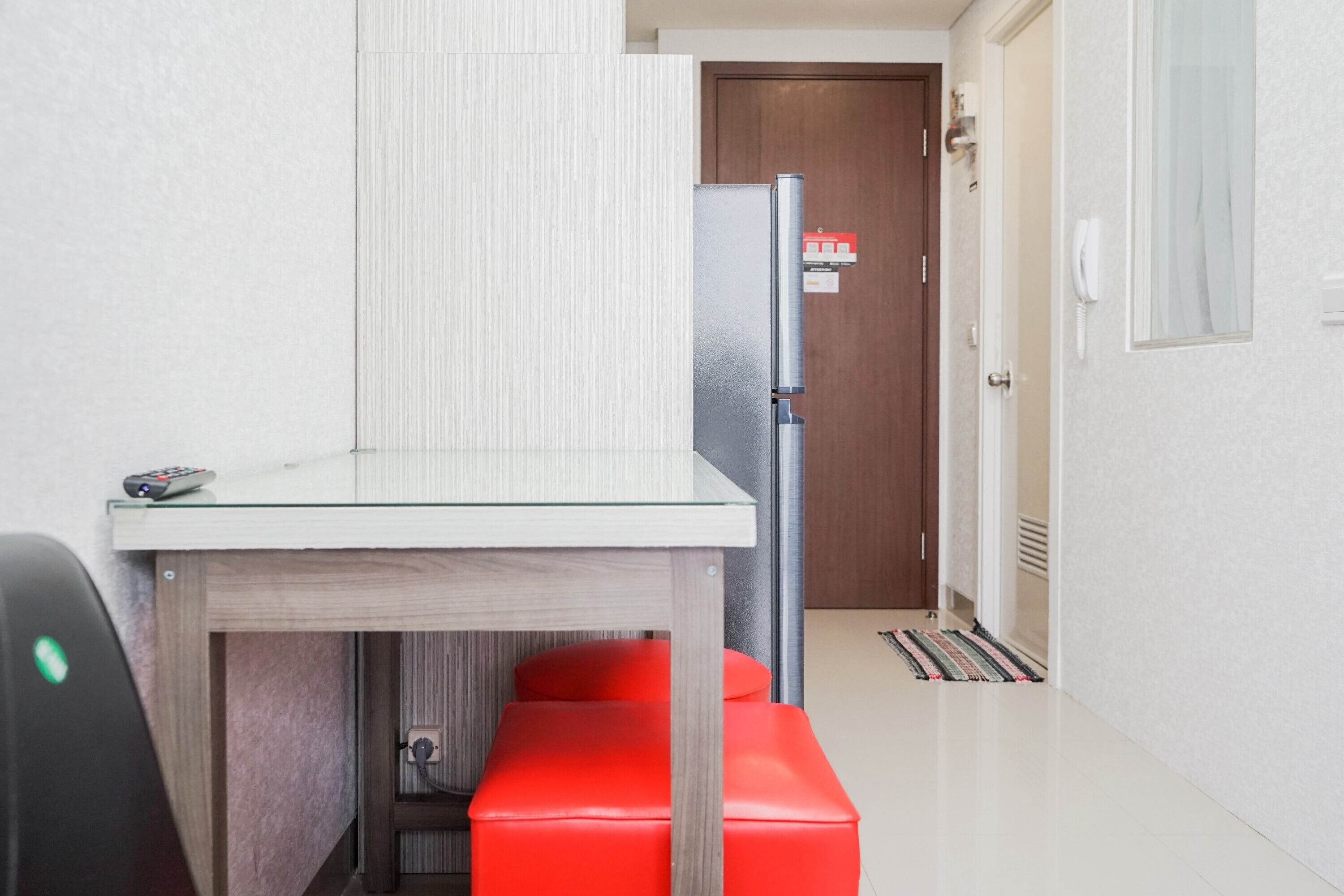 A compact kitchen with a refrigerator, a small table, and a red bench.