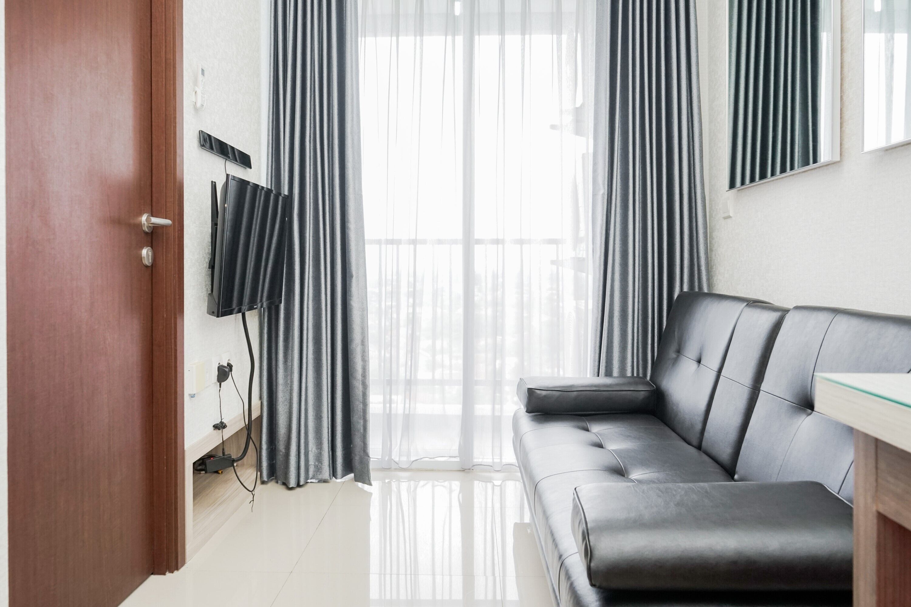 A modern living room with a leather sofa, a glass coffee table, and a TV mounted on the wall.