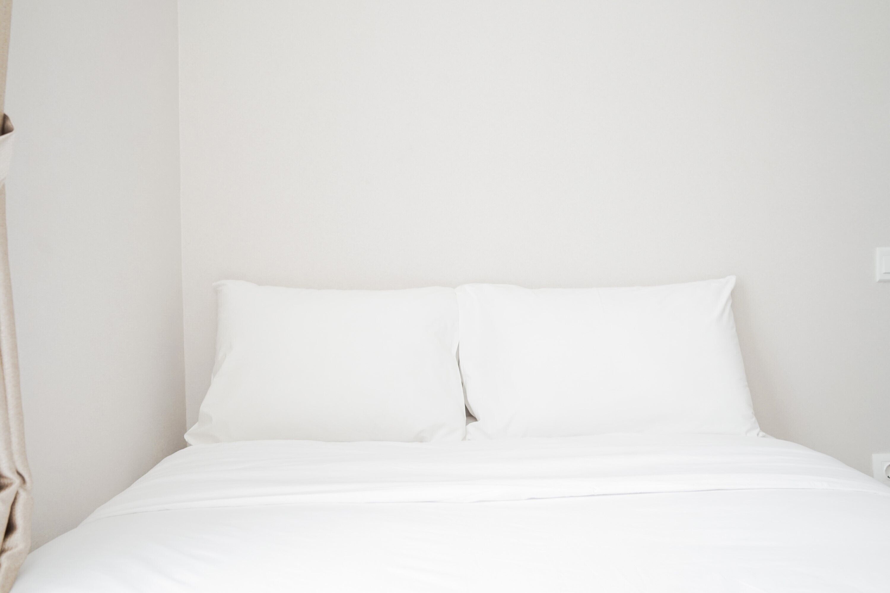 A neatly made bed with white linens in a room with plain white walls.