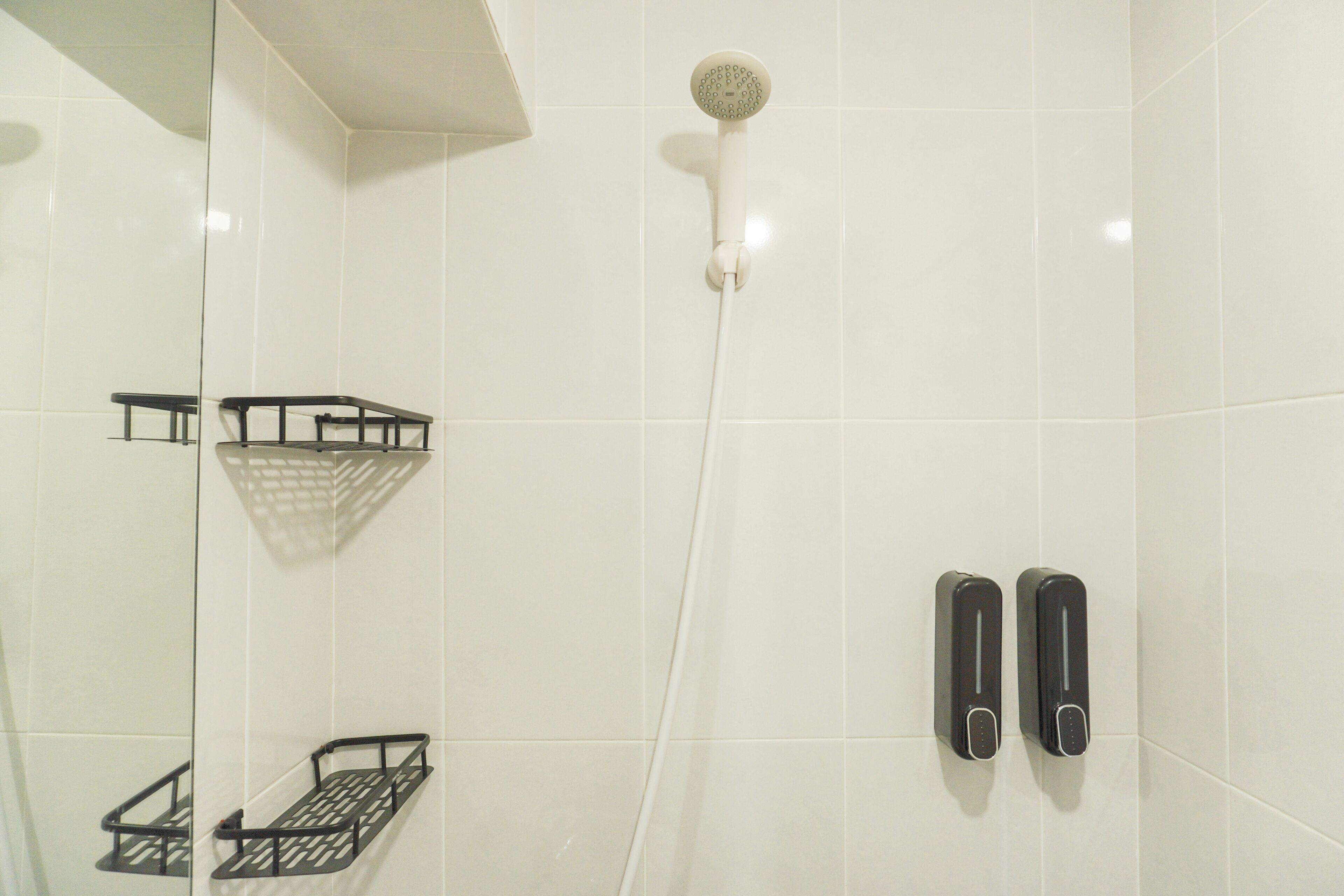 Douchegedeelte met een handdouche, een glazen scherm en twee zeepdispensers.