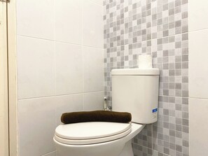 Des toilettes avec une cuvette blanche et une serviette marron posée sur le couvercle, le tout adossé à un mur orné de carreaux à motifs.