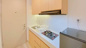 A compact kitchen with a built-in gas stove, a sink, and wooden cabinets. - Good Choice And Homey Studio At Tokyo Riverside Pik 2 Apartment (Teluknaga)