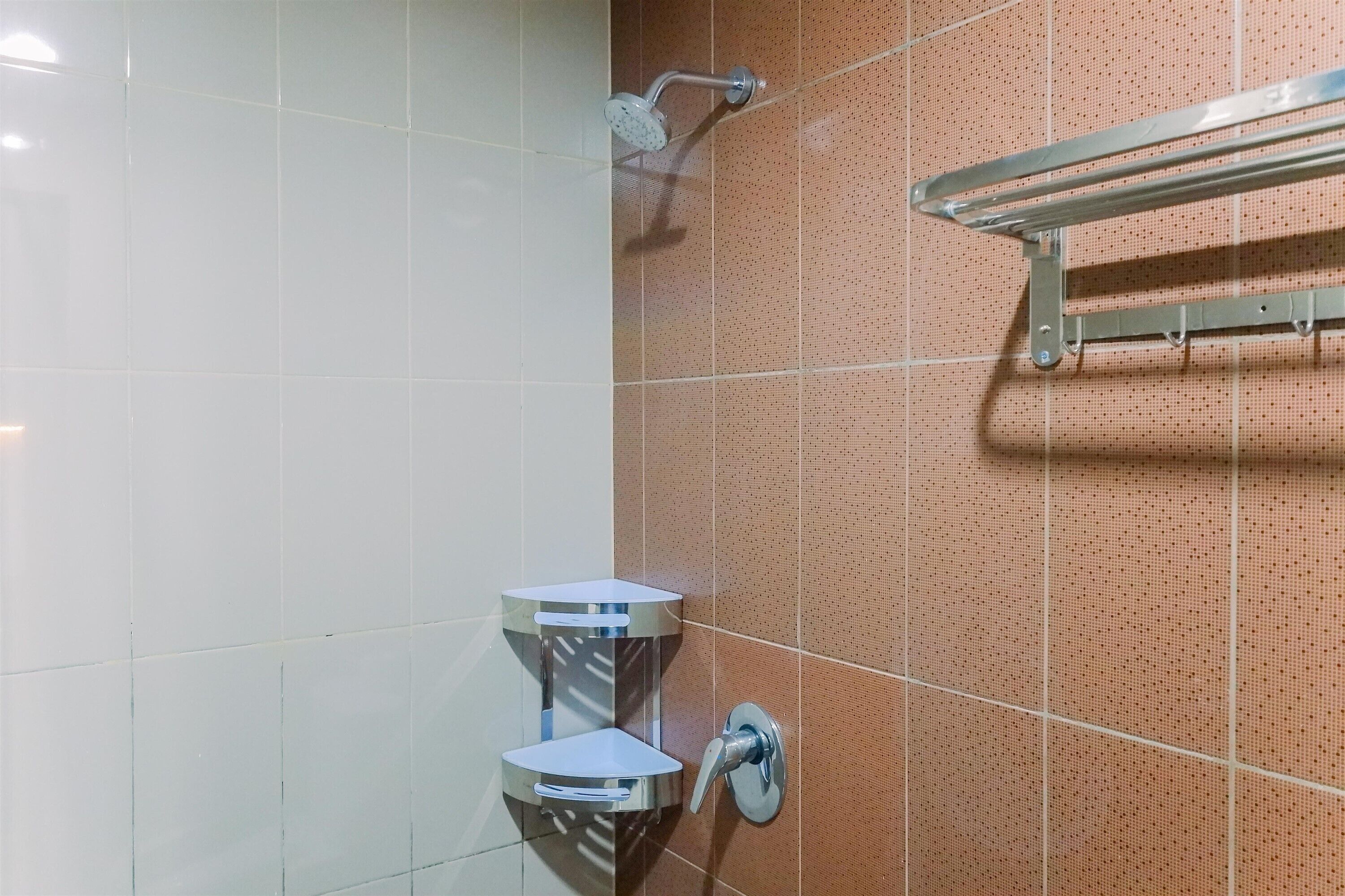 Ein Badezimmer mit weiß-braunen Fliesen, einer chromfarbenen Duschbrause und einem Handtuchhalter.