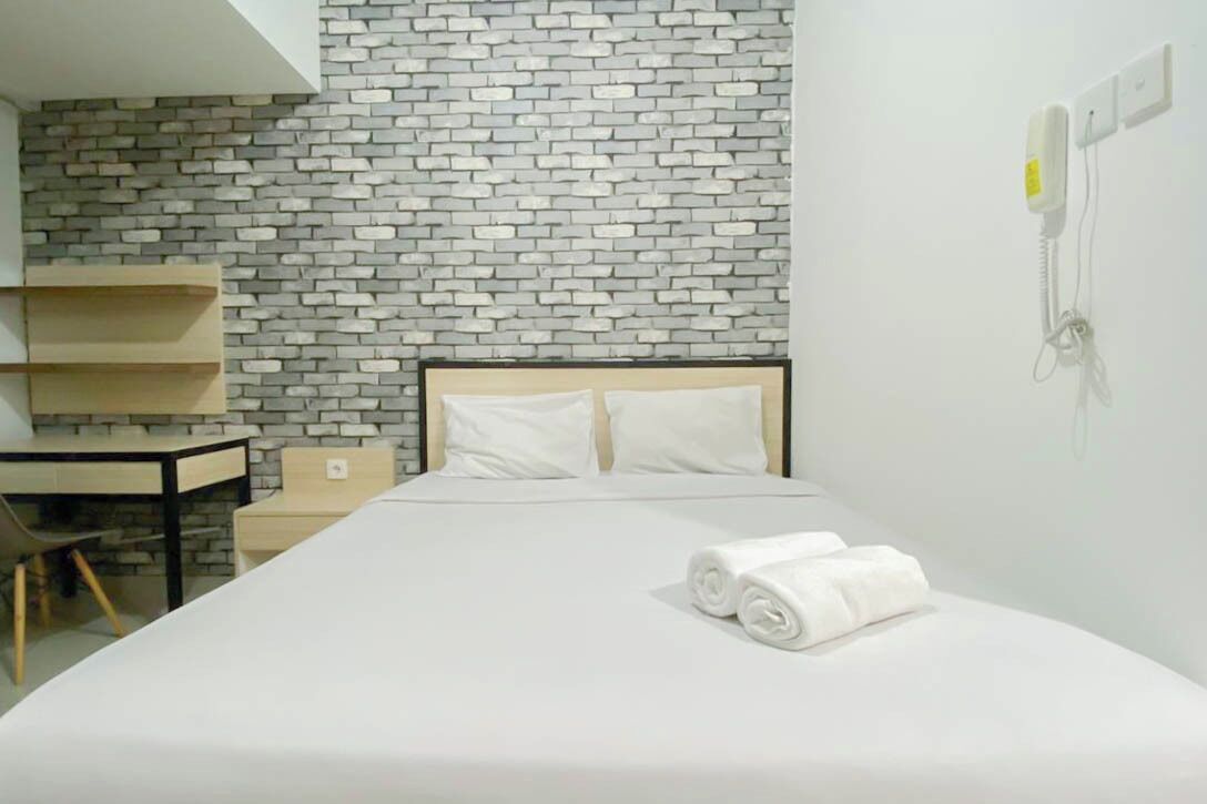 Une chambre d’hôtel avec un mur décoré d’un motif en briques, un lit avec du linge de maison blanc, un bureau et une chaise.