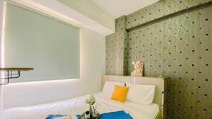 A hotel room with a bed, a window, a wall with a polka dot pattern, and a small shelf with decorative items.