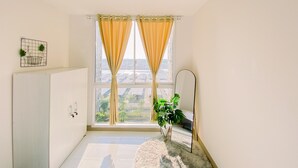 A bright room with a large window, a white cabinet, a mirror, and a potted plant. - Cozy 2Br Tokyo Riverside Pik 2 Apartment (Teluknaga)