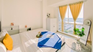 A hotel room with a bed, a desk, a wardrobe, a window with curtains, and a plant. - Cozy 2Br Tokyo Riverside Pik 2 Apartment (Teluknaga)