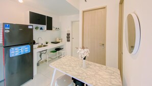 A compact kitchen with a black refrigerator, white cabinets, a small dining table, and a wooden door. - Cozy 2Br Tokyo Riverside Pik 2 Apartment (Teluknaga)