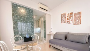 A modern living room with a grey sofa, white chairs, a small table with a water bottle, and a decorative wall panel. - The Signature Studio Apartment With Jaccuzi Art Deco (Bandung)