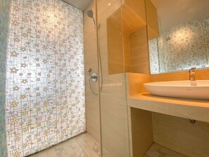 Bathroom features a tiled shower area with handheld showerhead and wall-mounted faucet, adjacent to a vanity with a large sink and mirror.