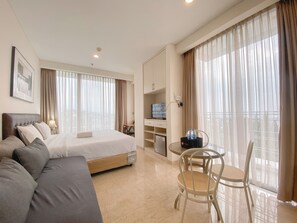 A hotel room with a bed, a sofa, a desk with a computer, and a dining area with chairs. - The Signature Studio Apartment With Jaccuzi Art Deco (Bandung)
