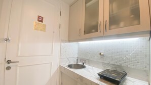 A compact kitchen with white cabinets, a stainless steel sink, and a marble countertop. - The Signature Studio Apartment With Jaccuzi Art Deco (Bandung)